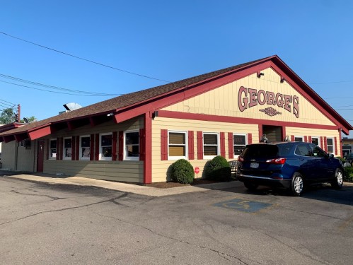 A colorful restaurant named "George's" with a red and yellow exterior, parked cars, and clear blue skies.