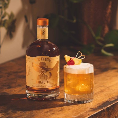 A bottle of Lyre's Amaretti non-alcoholic spirit next to a cocktail garnished with a lemon slice and cherry.