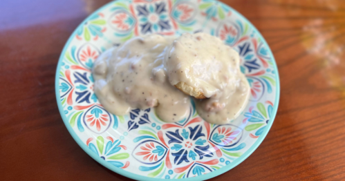 A colorful plate holds two biscuits smothered in creamy sausage gravy, set on a wooden table.