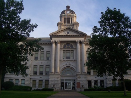 Historic courthouse with a clock tower, surrounded by trees and a grassy area, under a clear blue sky.