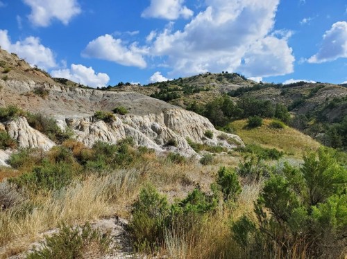 A scenic landscape featuring rocky hills, green vegetation, and a blue sky with fluffy clouds.