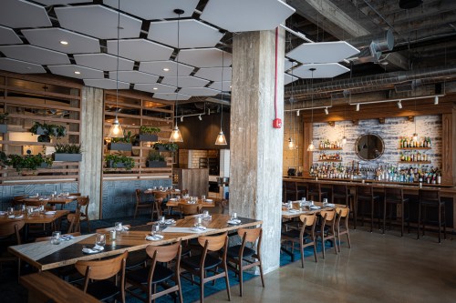 Modern restaurant interior featuring wooden tables, stylish lighting, and a well-stocked bar in a contemporary setting.