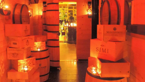 A dimly lit wine cellar with wooden barrels and stacked wine boxes, creating a warm, inviting atmosphere.