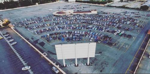 Aerial view of a large parking lot filled with cars arranged in rows, with a blank billboard in the foreground.