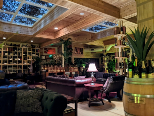 Cozy interior of a wine lounge with leather seating, wooden accents, and a skylight, featuring shelves of wine bottles.