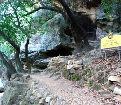 Entrance to Chumash Painted Cave State Park, featuring a rocky path and a sign near a cave entrance surrounded by trees.