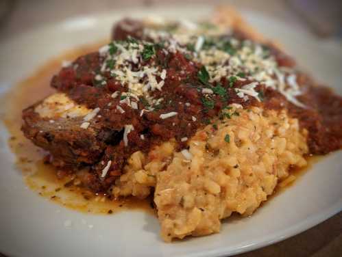 A plate of meatloaf topped with marinara sauce, served over creamy risotto and garnished with herbs and cheese.