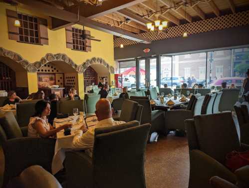 A spacious restaurant interior with green chairs, diners at tables, and large windows letting in natural light.