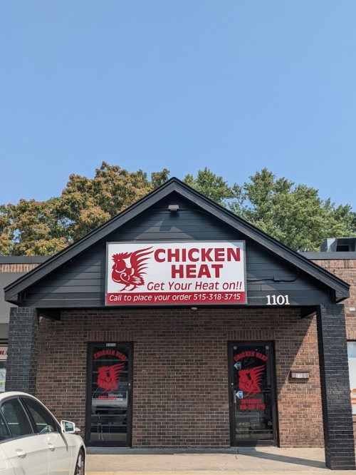 A storefront for "Chicken Heat" with a red logo, sign promoting heat and ordering, under a clear blue sky.