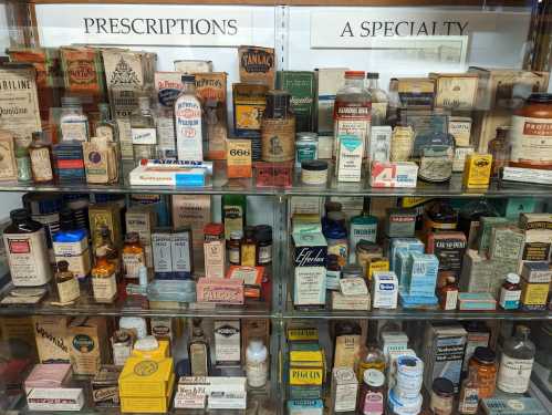 A display case filled with vintage medicine bottles and prescription boxes, showcasing various historical pharmaceutical products.