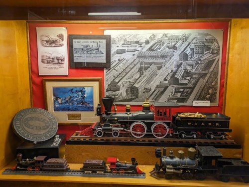 Display of vintage trains and historical documents in a wooden showcase, featuring a large steam locomotive model.