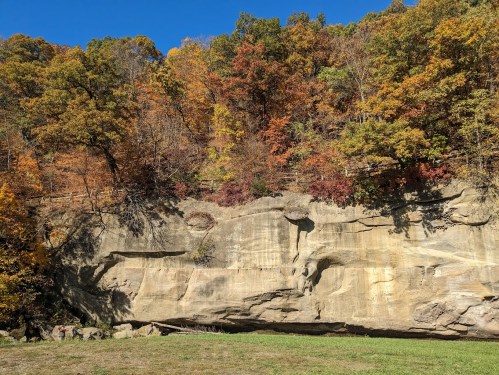 A rocky cliff surrounded by vibrant autumn foliage under a clear blue sky.