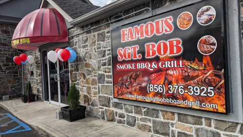 Sign for "Famous Sgt. Bob Smoke BBQ & Grill" featuring BBQ images, with red, white, and blue balloons outside.