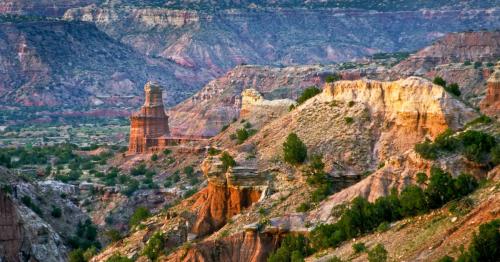 A scenic view of colorful canyons and rock formations under a clear sky, showcasing the beauty of a rugged landscape.