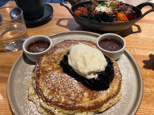 A plate of fluffy pancakes topped with whipped cream and berry compote, served with two small bowls of syrup.