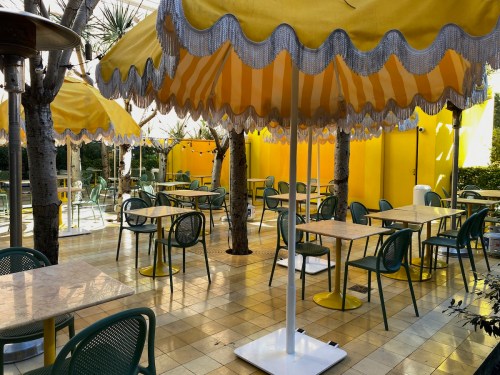 Bright outdoor café with yellow umbrellas, green chairs, and a sunny yellow wall, creating a cheerful atmosphere.