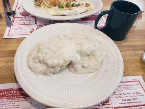 A plate of biscuits smothered in creamy sausage gravy, served with a green coffee mug in the background.