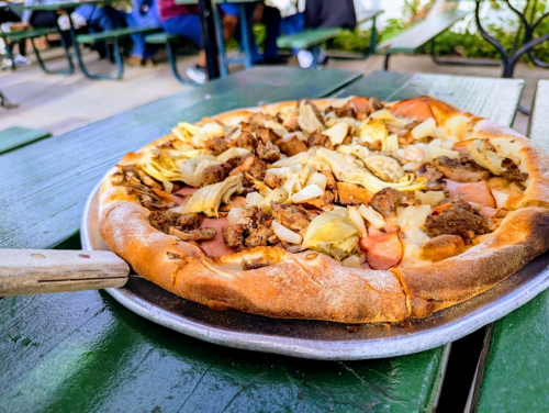 A freshly baked pizza topped with artichokes, sausage, and cheese on a green picnic table.