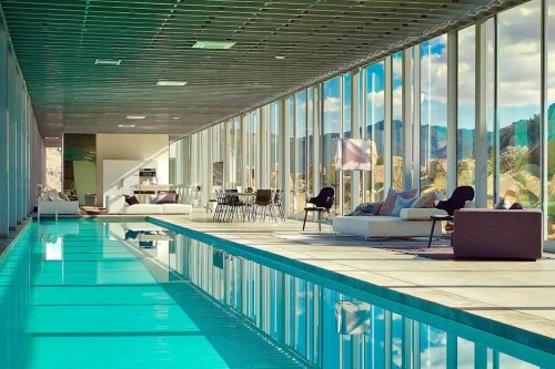 Modern indoor pool area with large windows, sleek furniture, and a view of mountains in the background.