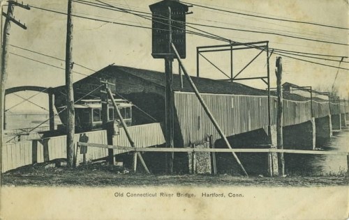 Black and white image of the Old Connecticut River Bridge in Hartford, with utility poles and structures nearby.
