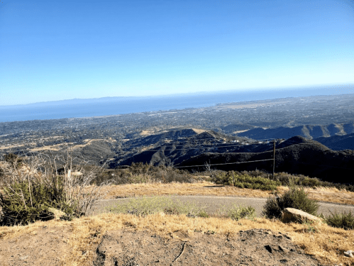 A panoramic view of a coastal landscape with mountains, valleys, and the ocean under a clear blue sky.