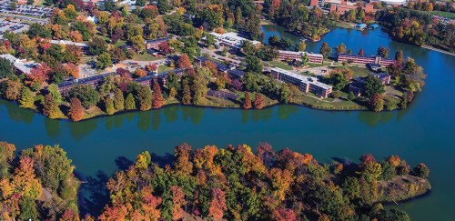 Aerial view of a vibrant autumn landscape with colorful trees surrounding a winding lake and buildings.