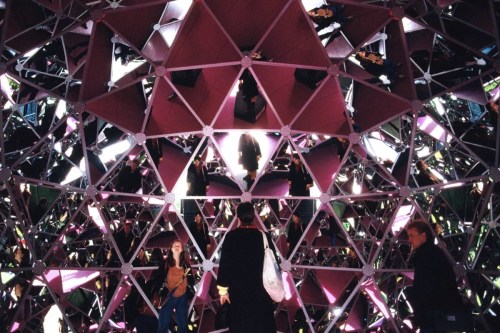 A geometric structure with mirrored surfaces reflecting people inside, creating a kaleidoscopic effect.