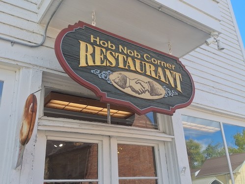 Sign for "Hob Nob Corner Restaurant" featuring a decorative design with two hands shaking.