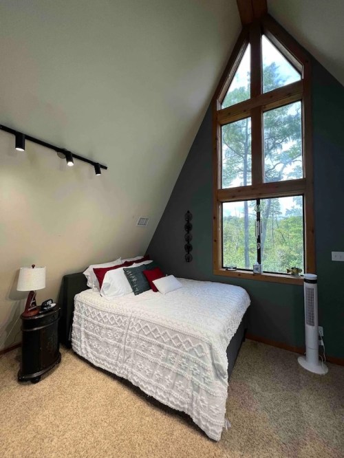 Cozy bedroom with a sloped ceiling, large window, and a bed adorned with white linens and red accents.