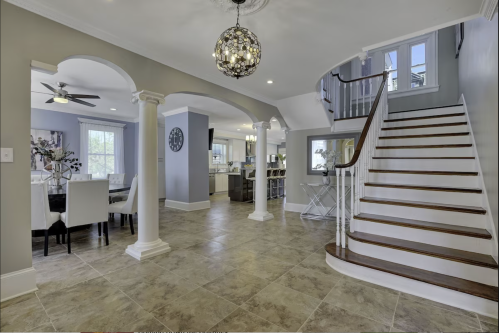 Spacious foyer with a staircase, dining area, and modern kitchen, featuring elegant lighting and tile flooring.