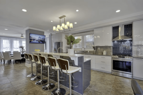 Modern kitchen with a large island, bar stools, stainless steel appliances, and a dining area in the background.