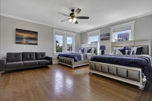 Spacious bedroom with two large beds, a gray sofa, and large windows letting in natural light.