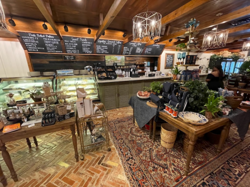 Cozy café interior featuring a display case, wooden tables, chalkboard menu, and plants in a warm, inviting atmosphere.