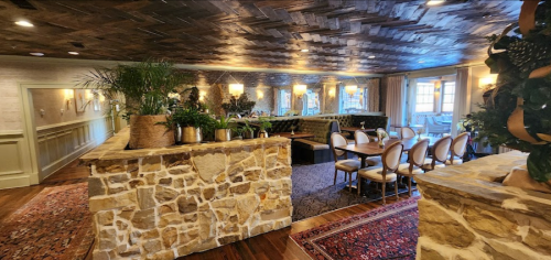 Cozy restaurant interior featuring stone walls, wooden ceiling, plants, and elegant dining tables.