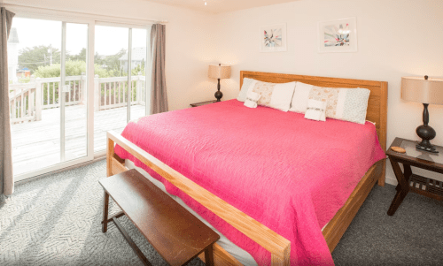 Cozy bedroom with a large bed, pink quilt, bedside tables, and sliding glass doors leading to a deck.