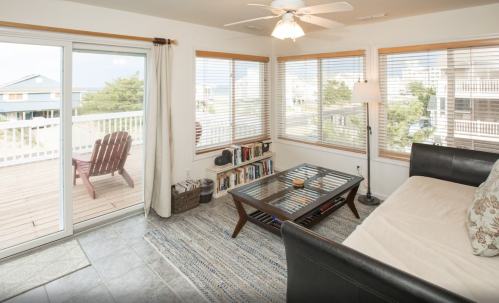 Cozy living room with large windows, a coffee table, a sofa, and a view of a deck and outdoor seating.