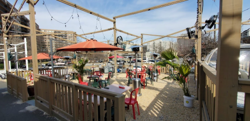Outdoor dining area with red chairs, umbrellas, and wooden structures, overlooking a waterfront view.