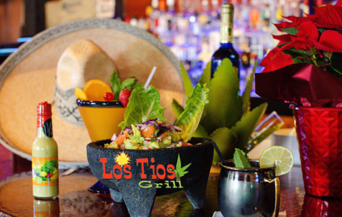 A vibrant display featuring a sombrero, a colorful drink, guacamole in a stone bowl, and festive decorations.