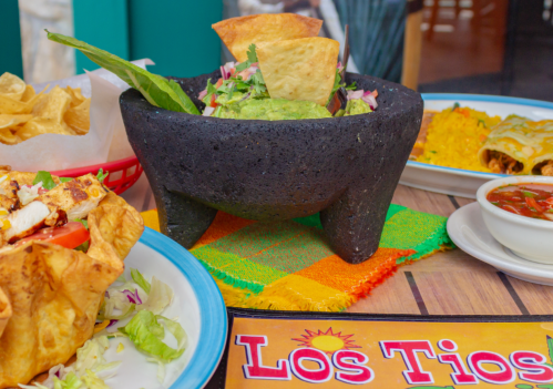 A vibrant table setting featuring a stone bowl of guacamole, tortilla chips, and colorful Mexican dishes.