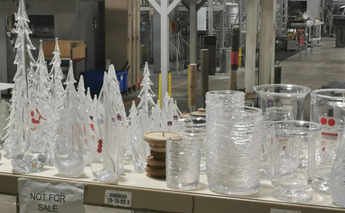 A display of various clear glass items, including decorative trees and vases, on a table in a warehouse setting.