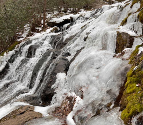 A cascading waterfall partially frozen, surrounded by rocky terrain and patches of snow and moss.