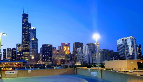 Chicago skyline at dusk, featuring tall buildings and the Willis Tower, illuminated against a blue sky.