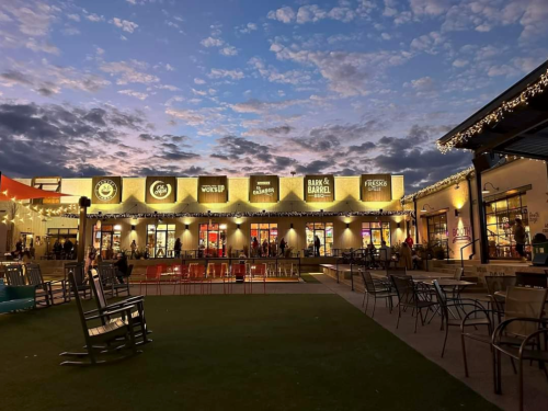 A vibrant outdoor shopping area at dusk, featuring various storefronts and a colorful sky with scattered clouds.