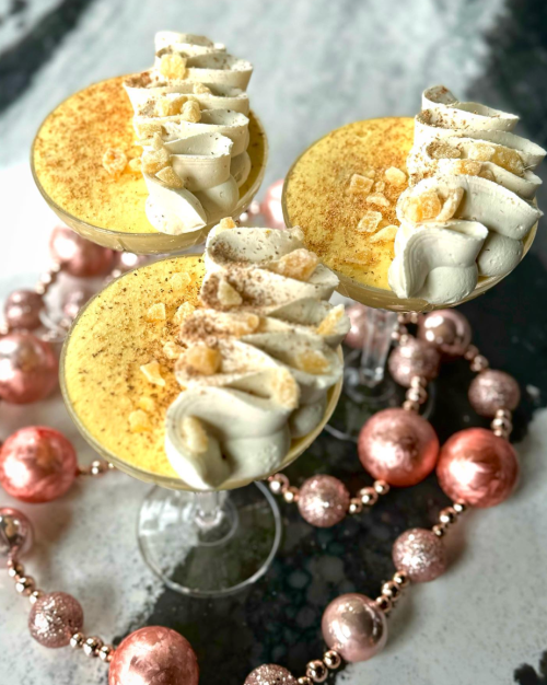 Three elegant dessert cups filled with creamy mousse, topped with whipped cream and garnished with crushed cookies, surrounded by pink ornaments.
