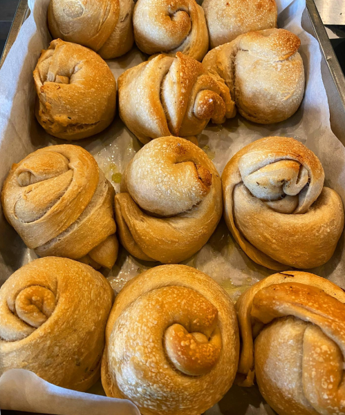 A tray of freshly baked, golden-brown, spiral-shaped bread rolls arranged neatly.