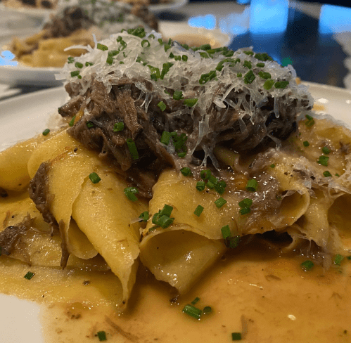 A plate of pappardelle pasta topped with shredded beef, grated cheese, and chopped chives in a savory sauce.