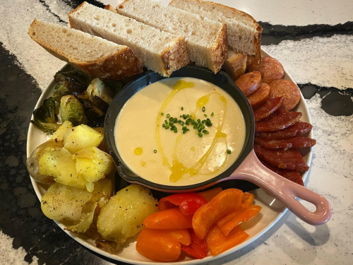 A platter featuring bread, creamy soup, roasted potatoes, sausage, Brussels sprouts, and colorful carrots.