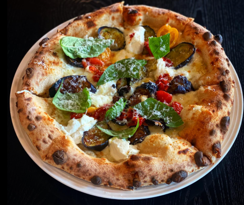 A freshly baked pizza topped with eggplant, tomatoes, spinach, and dollops of cheese on a golden crust.