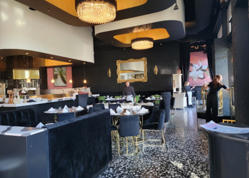 Elegant restaurant interior with black and gold decor, featuring tables, chairs, and a chandelier.