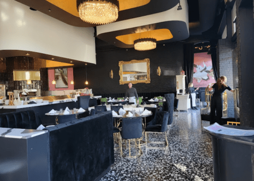 Elegant restaurant interior with black and gold decor, featuring tables, chairs, and a chandelier.